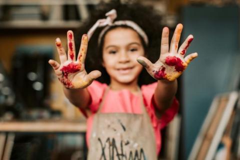 Girl in paint covered apron showing paint colored hands.