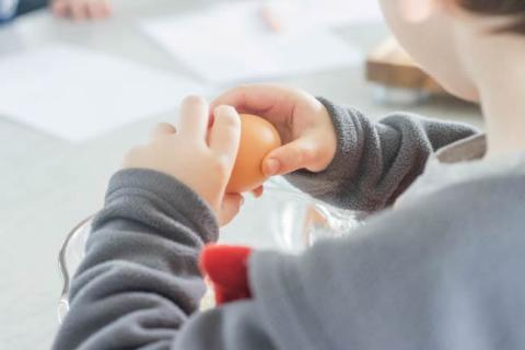 Young child cracking an egg in a glass bowl.