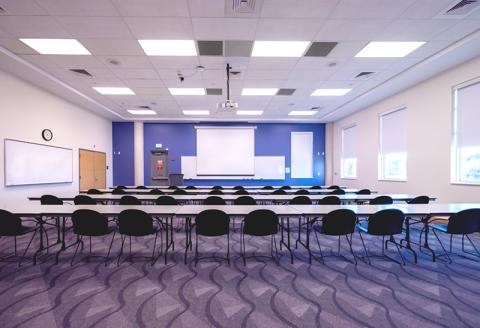 Tables and chairs facing whiteboard and projector screen in multipurpose room L211