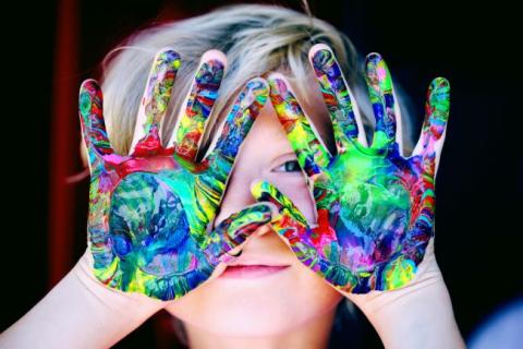 child with painted hands covering face