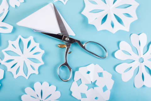 Paper snowflakes with open scissors lying across a folder page of paper.