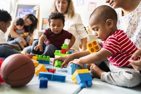 Four babies playing with blocks and three women.