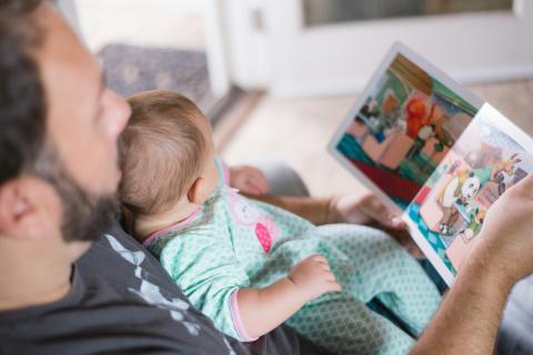 Man reading picture book with baby on his lap.