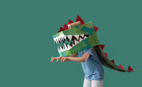 Child in dinosaur mask with arms raised like a t-rex.