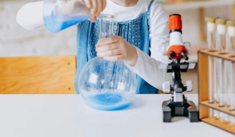 Child's hands pouring blue liquid into a science flask.