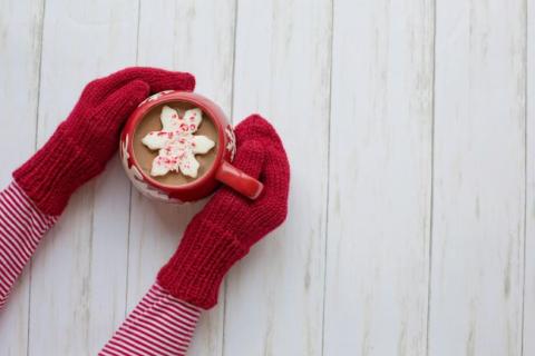 Overhead picture of person wearing red mittens holding a mug with hot cocoa and a snowflake shaped marshmallow.