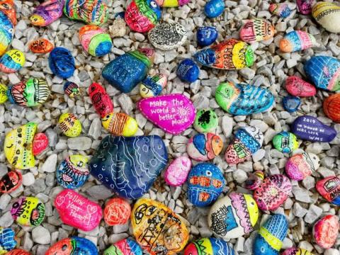 Brightly painted rocks with positive messages laying over plain rocks.