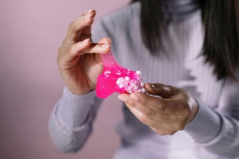 Women's hands playing with bright pink slime.