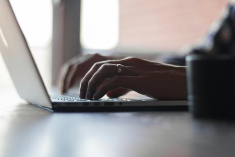 Hands typing on a laptop computer on a table surface.
