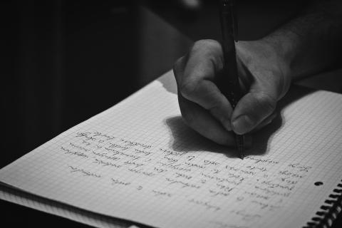 Black and white photo of hand writing in a notebook. 
