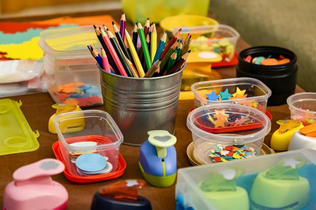 Table with silver bucket filled with colored pencils. Small plastic tubs with paper shapes.