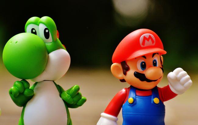 Two small plastic cartoon figurines- man with red hat and green dinosaur.