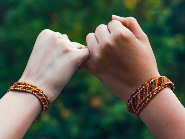 Hands making pinky promise with friendship bracelets on