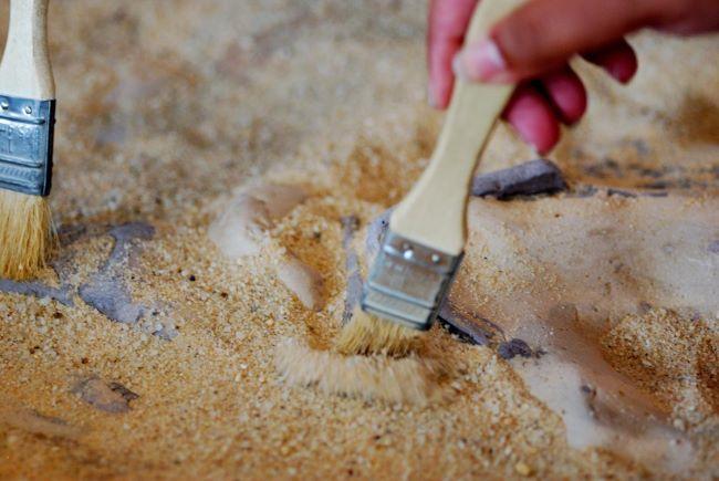 Paleontologist's hand using a small brush to uncover a fossil.