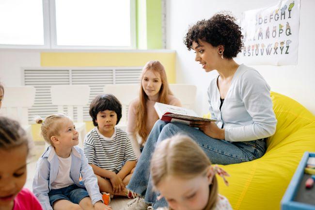 Group of children sitting on the floor listening to adult reading a book. 