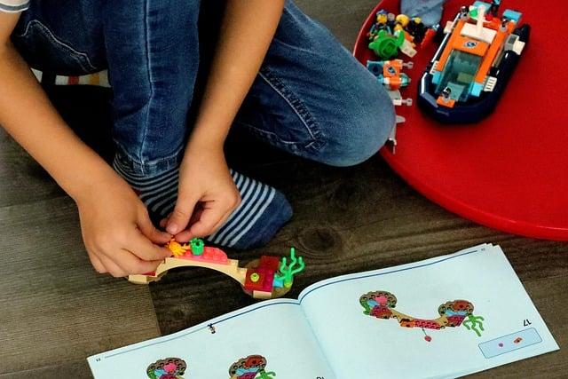 Child's hands constructing LEGO design with instructions.